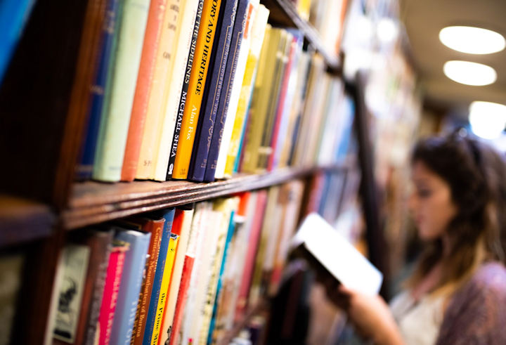 A person reading a book, standing next to bookshelves